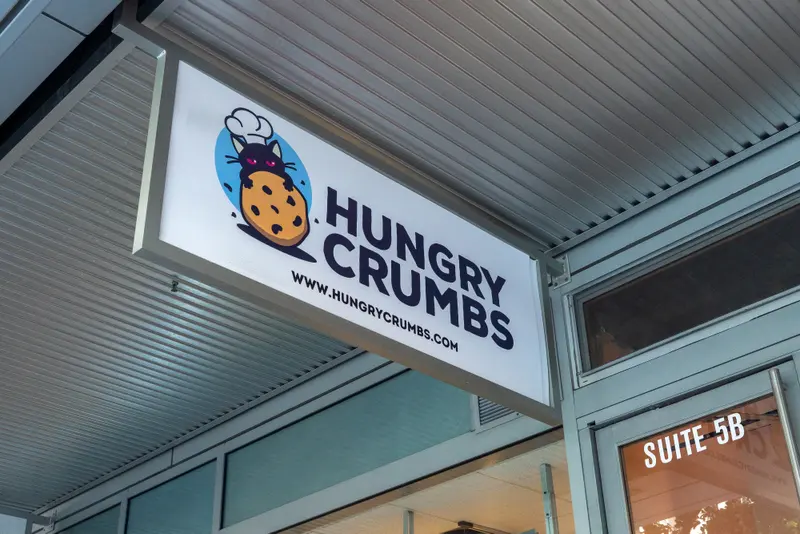 The Hungry Crumbs sign — a cat in a chef's hat behind a chocolate chip cookie — above the entrance to Suite 5B