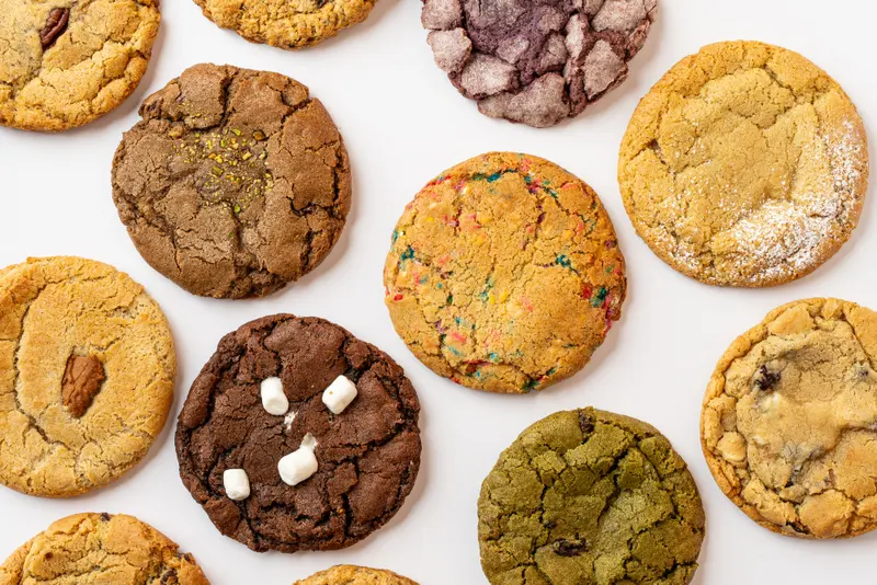 An overhead spread of Hungry Crumbs cookies on a white surface, several flavours side by side
