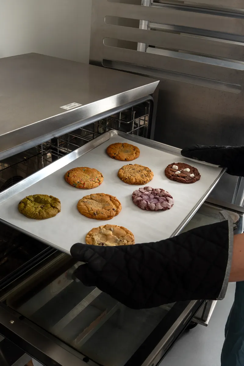 The kitchen: a baker in oven mitts sliding a tray of eight cookies out of the oven
