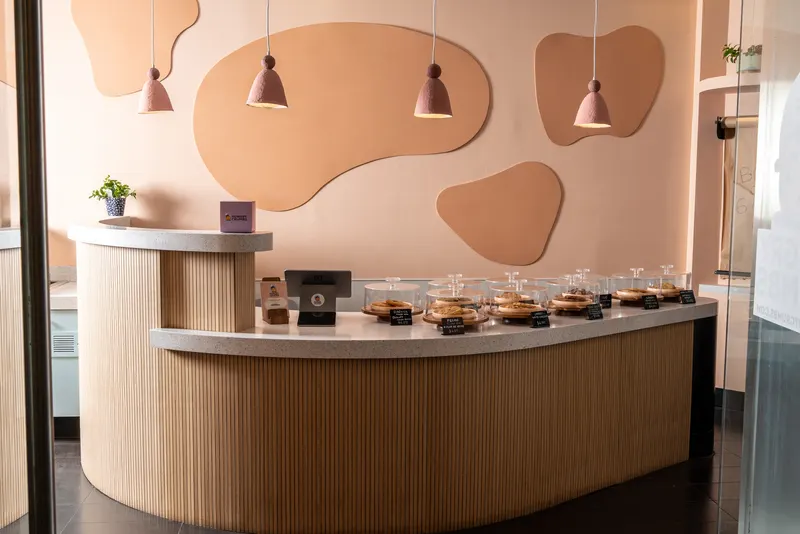 The full counter: a curved wooden base with a terrazzo top, cookies under glass domes, terracotta pendant lamps and tone-on-tone wall shapes behind